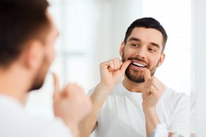 Man flossing his teeth in the mirror